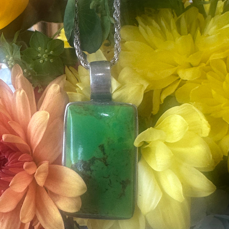 Green pendant on a chain surrounded by yellow and pink flowers